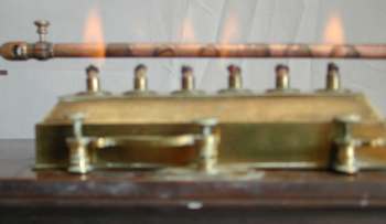 Galleria d'immagini relative alla verifica del funzionamento dell'Apparecchio per la dilatazione lineare dei metalli, Malfi, &copy; D 2003. Foto 1: accensione degli stoppini; foto 2: posizionamento del serbatoio sotto alla sbarretta di rame; foto 3, 4 e 5: il progressivo movimento dell'indice sul quadrante graduato.